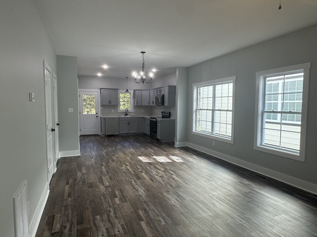 unfurnished living room with sink, an inviting chandelier, a wealth of natural light, and dark hardwood / wood-style floors