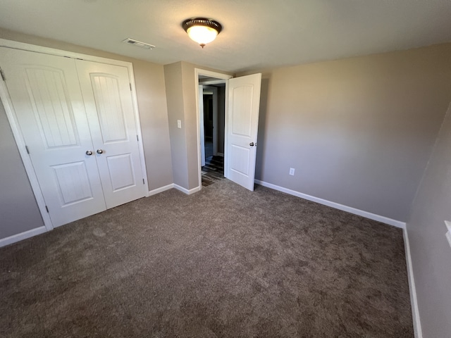 unfurnished bedroom with dark colored carpet and a closet