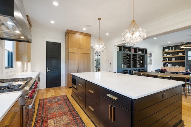 kitchen featuring a kitchen island, extractor fan, decorative light fixtures, light wood-type flooring, and appliances with stainless steel finishes