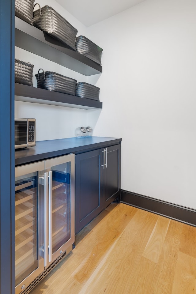 bar featuring blue cabinetry, light hardwood / wood-style floors, and beverage cooler