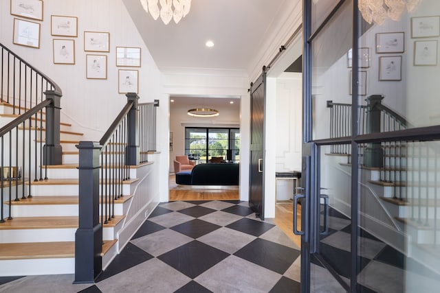 staircase with ornamental molding, hardwood / wood-style floors, a barn door, and an inviting chandelier