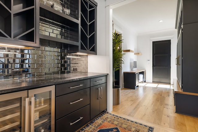 bar featuring backsplash, wine cooler, light wood-type flooring, and dark stone countertops