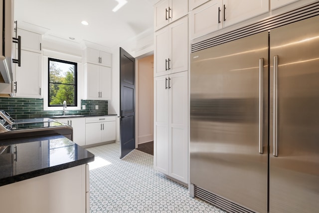 kitchen featuring white cabinets, stove, backsplash, and built in refrigerator