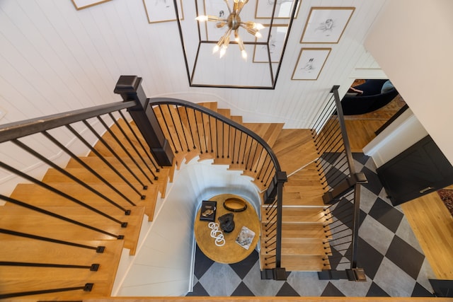 stairs with a notable chandelier, wooden walls, and wood-type flooring