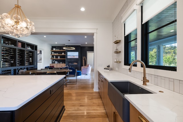 kitchen featuring sink, pendant lighting, light wood-type flooring, light stone counters, and tasteful backsplash