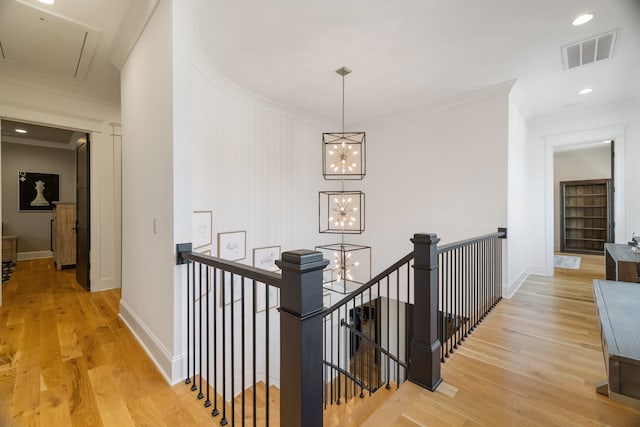 corridor featuring an inviting chandelier, ornamental molding, and light wood-type flooring