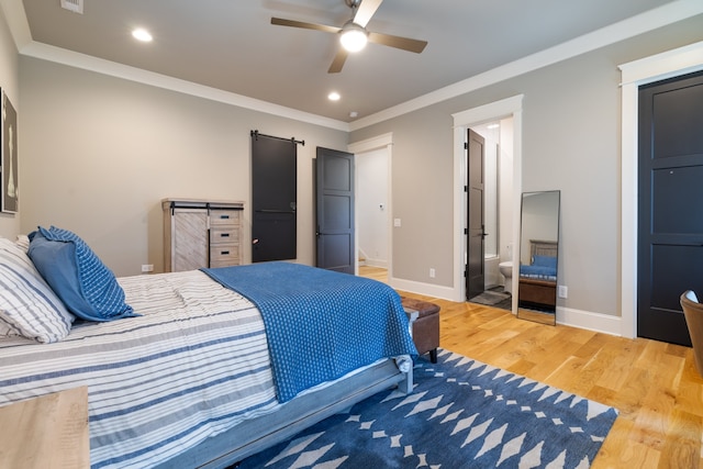 bedroom with ceiling fan, hardwood / wood-style flooring, a barn door, ornamental molding, and ensuite bath