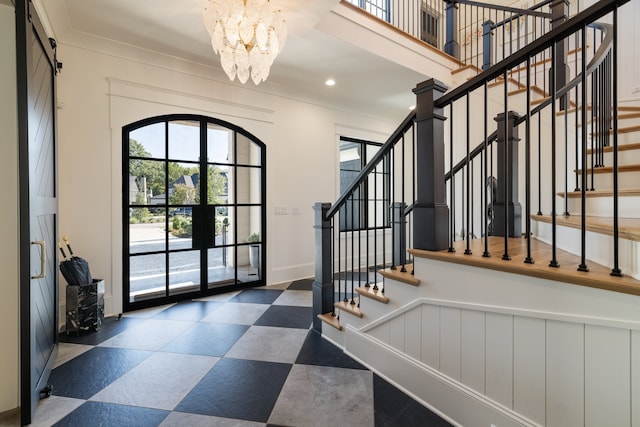 foyer featuring french doors, ornamental molding, a barn door, and a notable chandelier