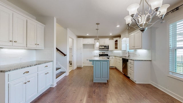 kitchen featuring white cabinets, a kitchen island, appliances with stainless steel finishes, light stone countertops, and light wood-type flooring