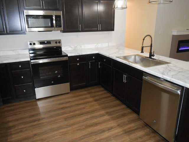 kitchen featuring dark wood-type flooring, sink, light stone countertops, kitchen peninsula, and stainless steel appliances