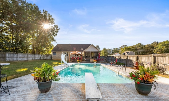 view of swimming pool featuring a patio, a water slide, a yard, and a diving board