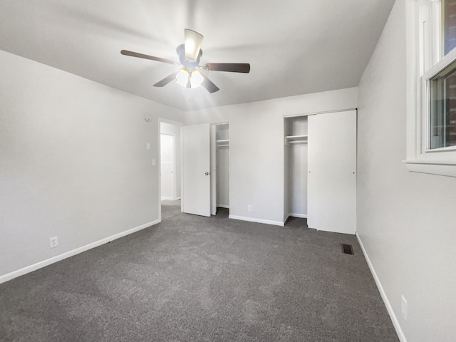 unfurnished bedroom featuring ceiling fan, multiple closets, and dark carpet