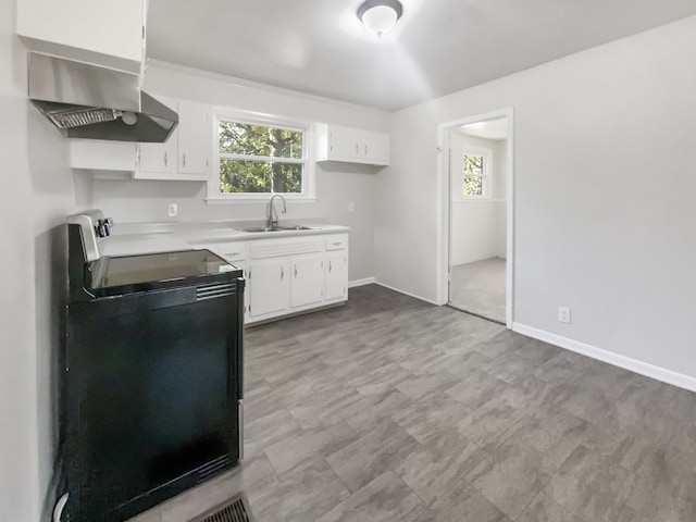 kitchen with wall chimney exhaust hood, range, white cabinets, and sink