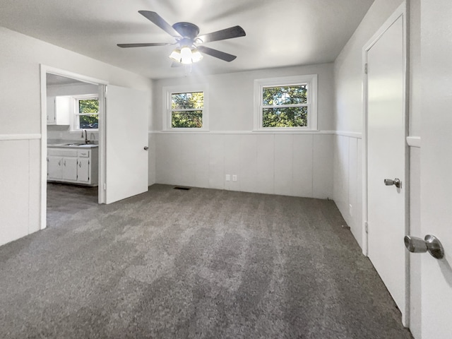 unfurnished bedroom featuring ensuite bathroom, sink, dark carpet, and ceiling fan