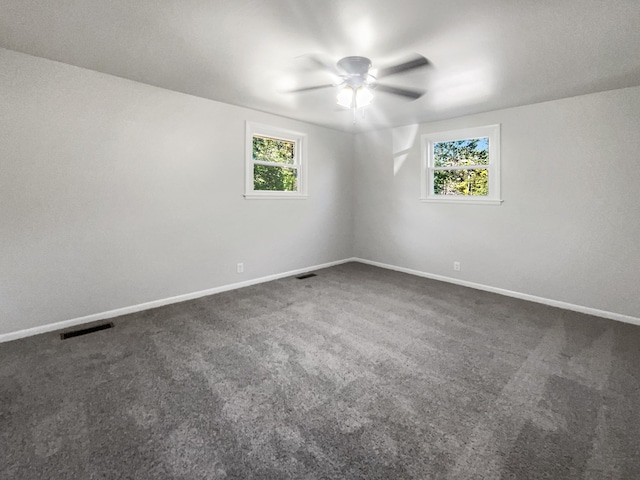 spare room with a wealth of natural light and dark colored carpet