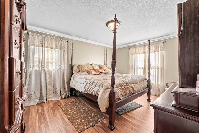 bedroom featuring ornamental molding, light hardwood / wood-style flooring, and a textured ceiling