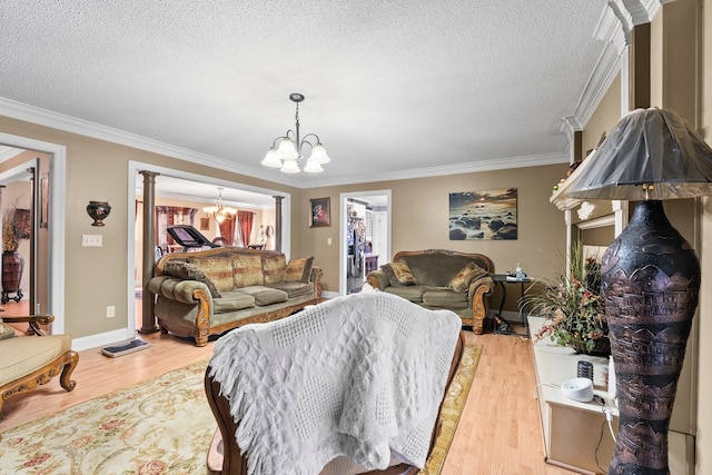 living room featuring decorative columns, crown molding, an inviting chandelier, a textured ceiling, and light hardwood / wood-style floors