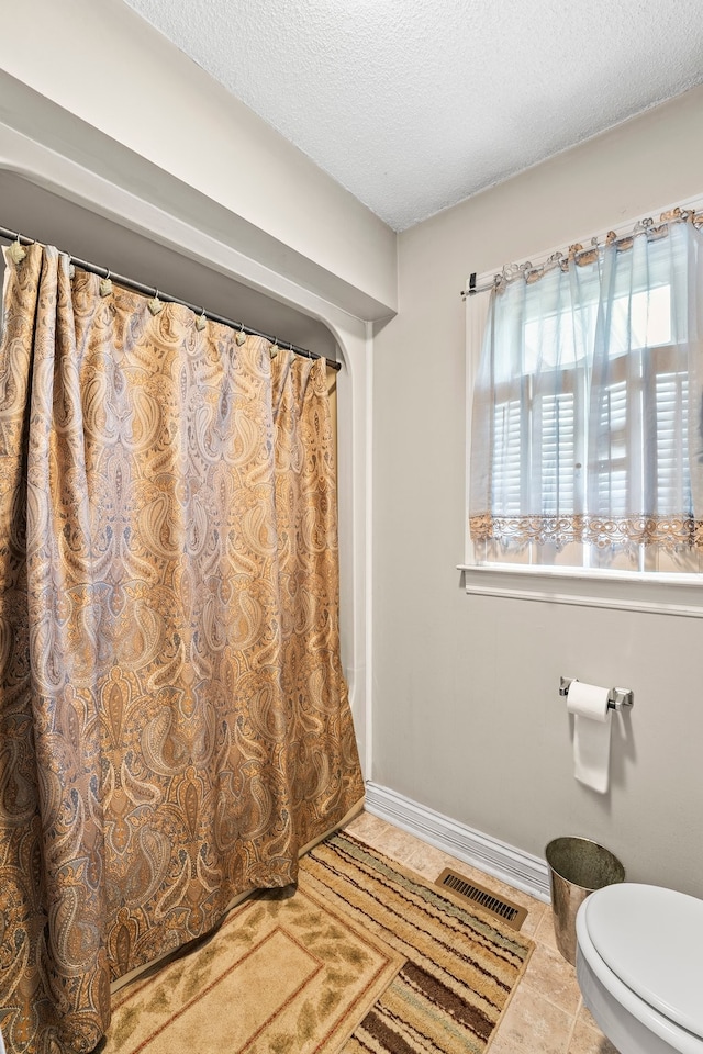 bathroom featuring toilet, a textured ceiling, a shower with curtain, and tile patterned flooring