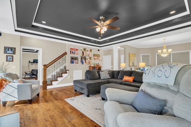 living room featuring wood-type flooring, a tray ceiling, ornamental molding, ceiling fan with notable chandelier, and ornate columns