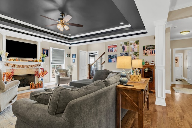 living room with a raised ceiling, decorative columns, crown molding, a premium fireplace, and light hardwood / wood-style flooring