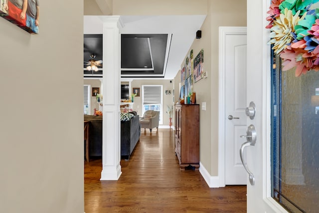 hallway featuring dark wood-type flooring, ornate columns, and a tray ceiling