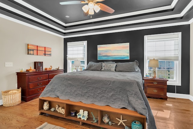 bedroom with ceiling fan, a tray ceiling, ornamental molding, and light hardwood / wood-style flooring