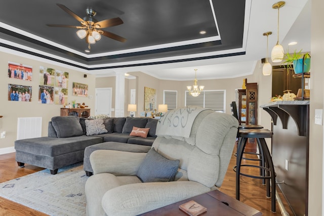 living room with ornate columns, a raised ceiling, wood-type flooring, and ceiling fan with notable chandelier