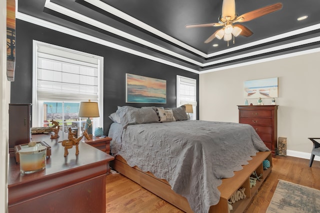 bedroom with ornamental molding, a tray ceiling, light wood-type flooring, and ceiling fan