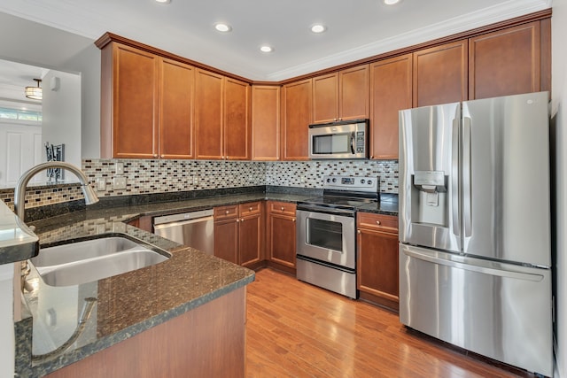 kitchen featuring dark stone countertops, appliances with stainless steel finishes, light hardwood / wood-style flooring, and sink