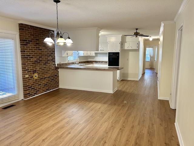 kitchen featuring oven, a textured ceiling, kitchen peninsula, white cabinetry, and light hardwood / wood-style floors