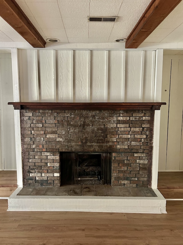 room details featuring beam ceiling, hardwood / wood-style floors, a brick fireplace, and a textured ceiling