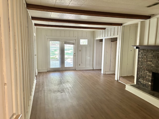 unfurnished living room featuring beam ceiling, a brick fireplace, and hardwood / wood-style flooring