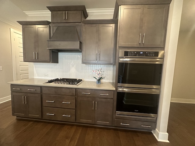 kitchen with decorative backsplash, appliances with stainless steel finishes, custom range hood, dark wood-type flooring, and crown molding