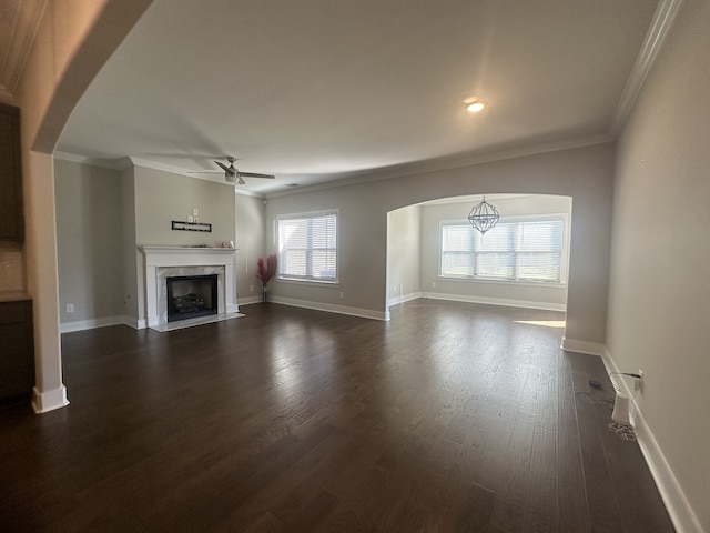 unfurnished living room featuring ceiling fan with notable chandelier, dark hardwood / wood-style flooring, and ornamental molding