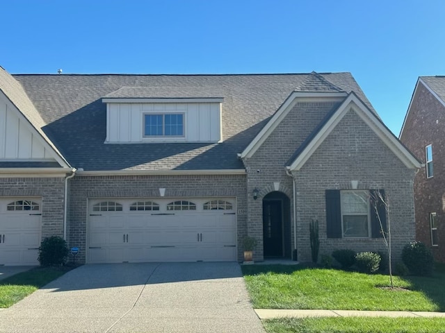 view of front of home featuring brick siding, driveway, roof with shingles, board and batten siding, and a front yard