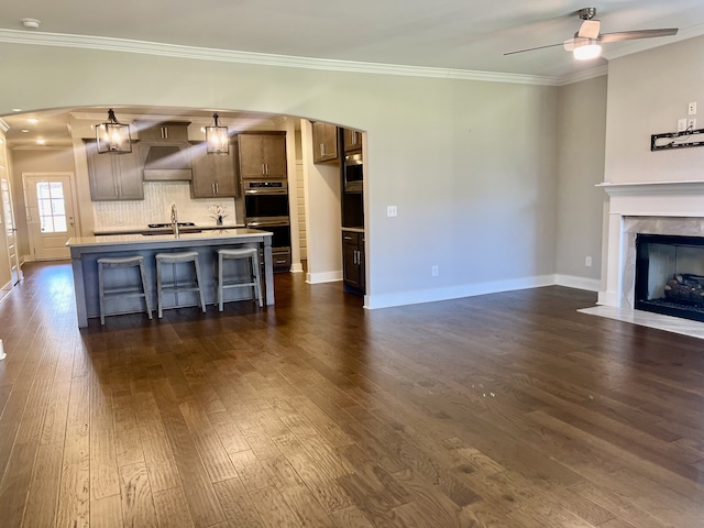 unfurnished living room featuring ceiling fan, dark hardwood / wood-style flooring, sink, and crown molding