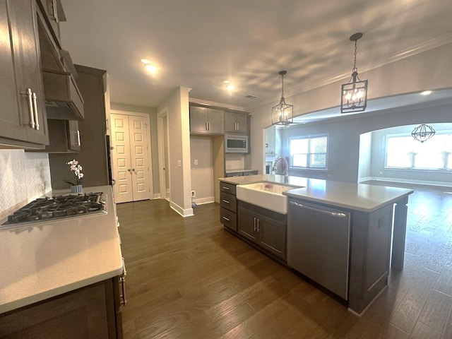 kitchen with sink, dark wood-type flooring, stainless steel appliances, decorative light fixtures, and a kitchen island with sink