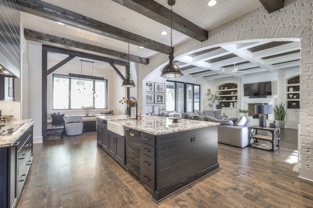 kitchen with a kitchen island with sink, sink, light stone countertops, and pendant lighting