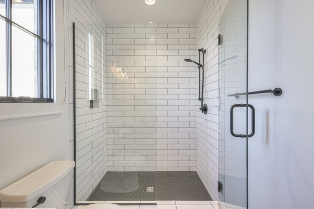 bathroom featuring a shower with door, toilet, and a wealth of natural light