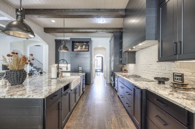 kitchen featuring beam ceiling, hanging light fixtures, dark hardwood / wood-style flooring, cooktop, and light stone counters