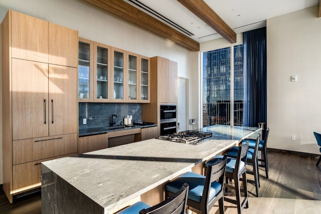 kitchen with beam ceiling, tasteful backsplash, a kitchen island, dark hardwood / wood-style floors, and stainless steel gas cooktop