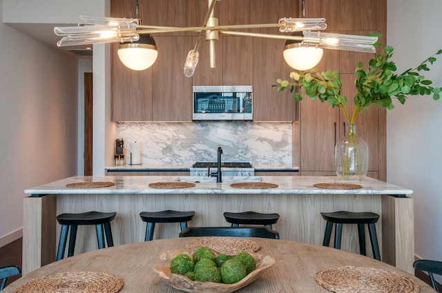 kitchen with a center island with sink, backsplash, a kitchen bar, pendant lighting, and stainless steel appliances