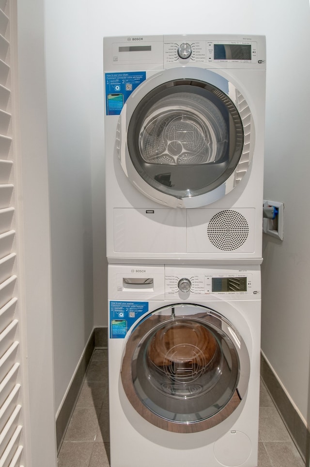 washroom featuring stacked washer and clothes dryer and dark tile patterned flooring