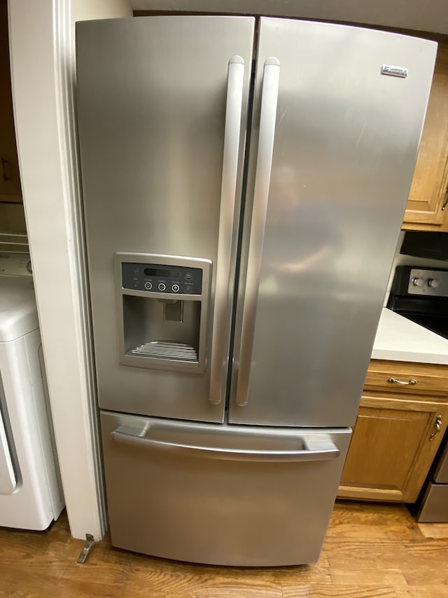 interior details with stainless steel fridge, washer / dryer, light hardwood / wood-style floors, and range