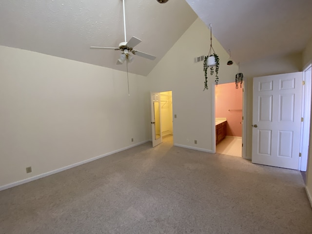 unfurnished bedroom with connected bathroom, ceiling fan, high vaulted ceiling, light colored carpet, and a walk in closet