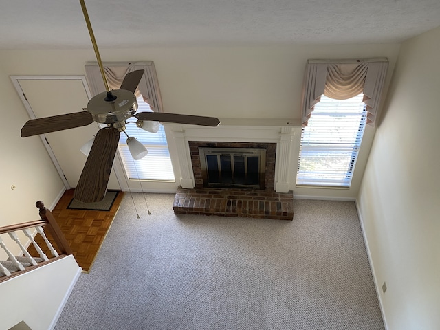 unfurnished living room featuring carpet flooring, ceiling fan, a fireplace, and a textured ceiling