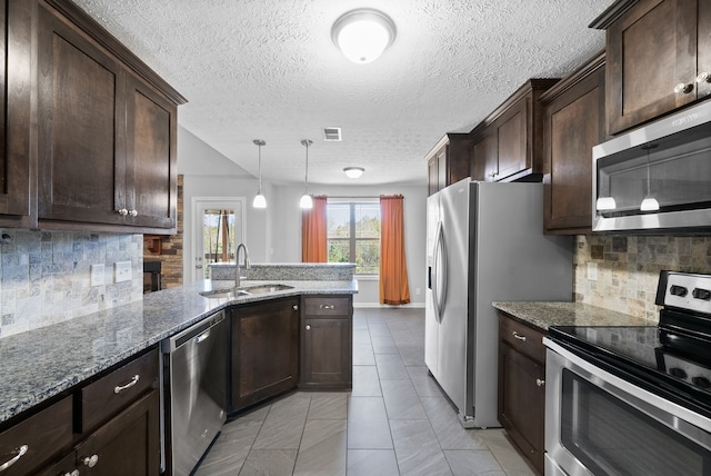 kitchen with sink, stainless steel appliances, pendant lighting, dark stone countertops, and decorative backsplash