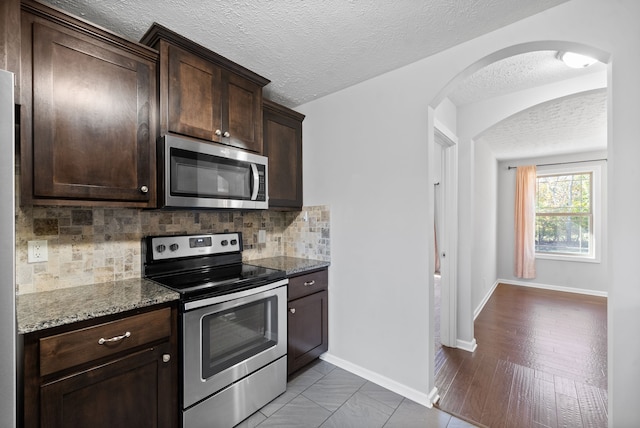 kitchen with stainless steel appliances, dark brown cabinetry, stone counters, a textured ceiling, and light hardwood / wood-style floors