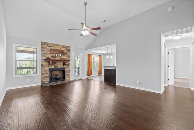 unfurnished living room featuring dark wood-type flooring, ceiling fan, high vaulted ceiling, and a stone fireplace