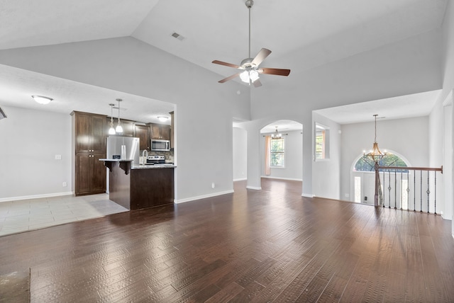 unfurnished living room with high vaulted ceiling, hardwood / wood-style flooring, and ceiling fan with notable chandelier